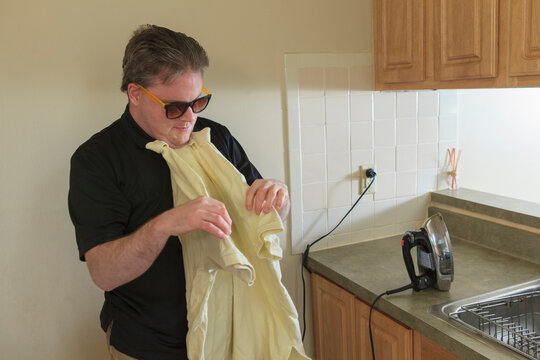 Man with congenital blindness folding his shirt after ironing it at home