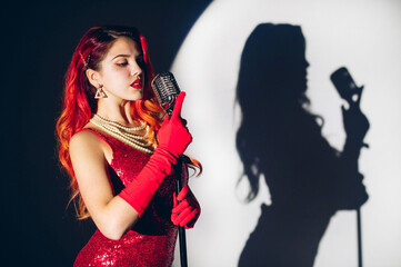 Pretty woman in red shiny dress with a red hair holding micropho