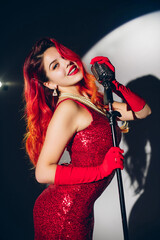 Pretty woman in red shiny dress with a red hair holding micropho