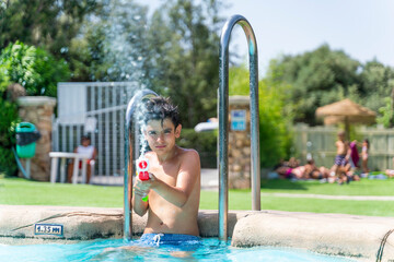Dark-haired boy playing with the water gun in the pool