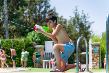 Dark-haired boy playing with the water gun in the pool