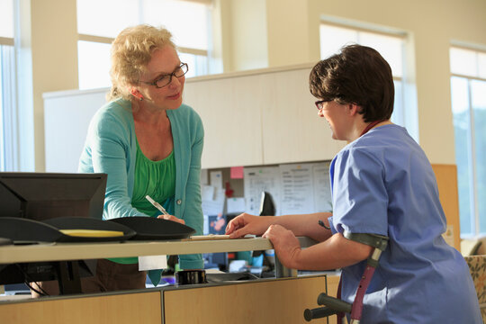 Nurse with Cerebral Palsy checking with administration about a patient's records in a clinic