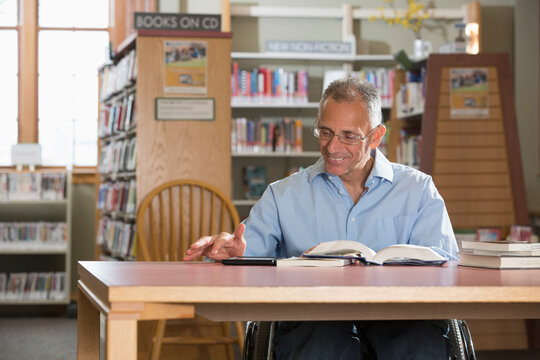 Man with a Spinal Cord Injury in a library reading a tablet