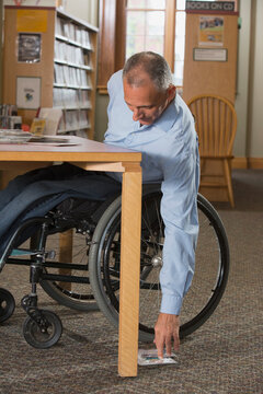 Man in a wheelchair with a Spinal Cord Injury in a library reaching for DVDs