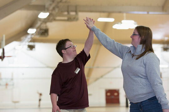 Young man with Down Syndrome doing a High-Five with student in gym
