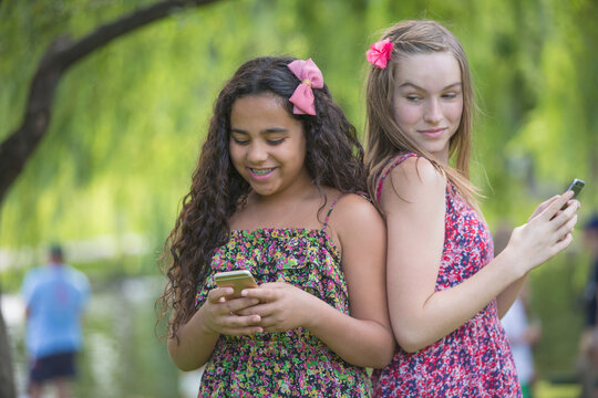 Two Hispanic teen sisters with braces looking at their cell phones in park