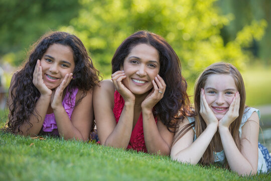 Portrait of happy Hispanic mother with two teen daughters wearing braces and smiling in a park