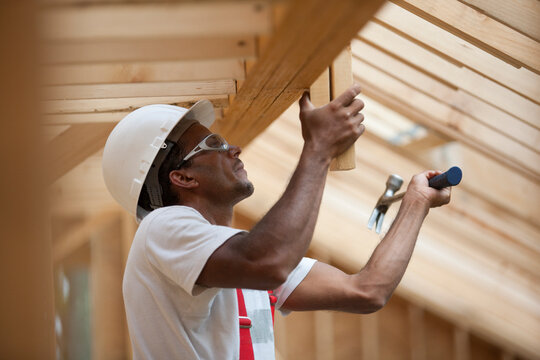Hispanic carpenter hammering boards on roofing at a house under construction