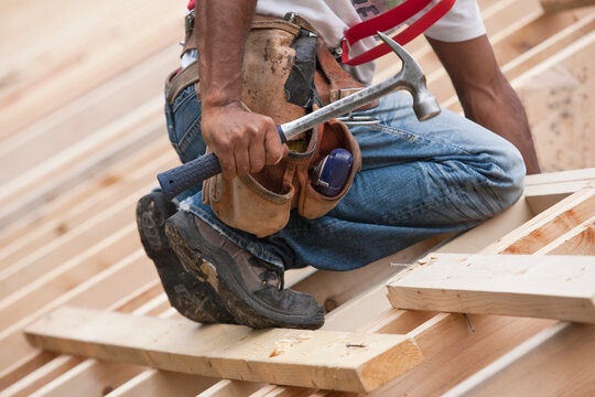 Carpenter with a hammer and tool belt on the roof at a house under construction
