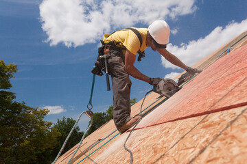 Hispanic carpenter using a circular saw on a roof sheathing at a house under construction