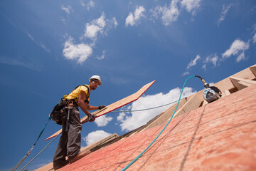 Carpenter installing 'L' shape panel on the roof of a house under construction