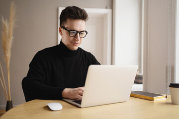 Fototapeta premium A young freelance man working at a workplace uses a laptop, prints an online text message.