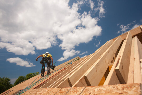 Carpenter holding a nail gun on the roof of a house under construction