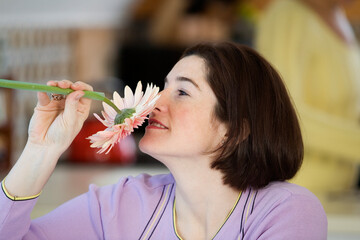 A woman smelling a daisy.