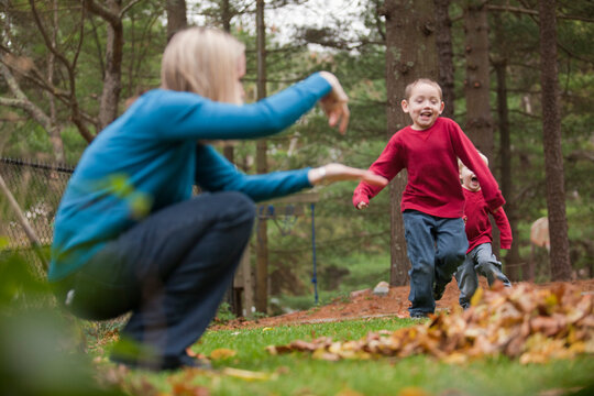 Mother signing to her son to jump in a pile of leaves as he runs in a park towards her