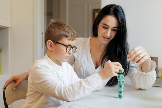 Un educatrice compie delle attivit&agrave; didattiche con un bambino biondo seduti di fronte alla scrivania di uno studio 