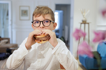 bambino mangia un panino con hamburger all'interno di una casa 