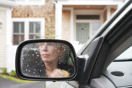 Woman's image reflected on the rearview mirror of a car.