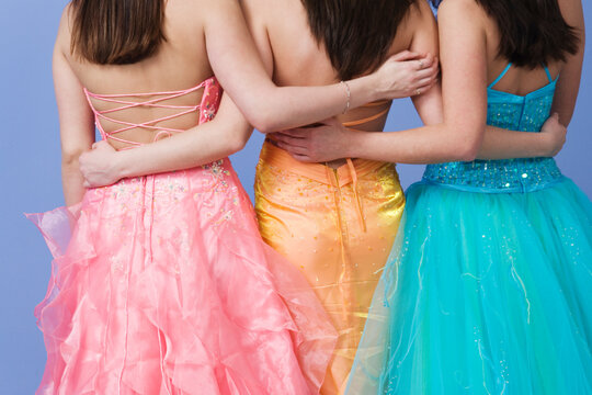 Friends holding each other by the waist wearing prom dresses.