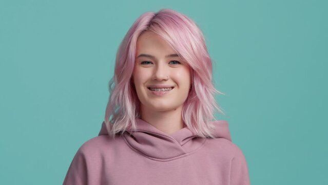 Slow motion close up cool funky girl with trendy pastel pink hair color showing tongue. Young playful hipster woman flirting looking straight at camera. Portrait girl with piercing and teeth brackets