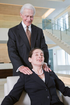 View of businessman giving shoulder massage to executive in an office.