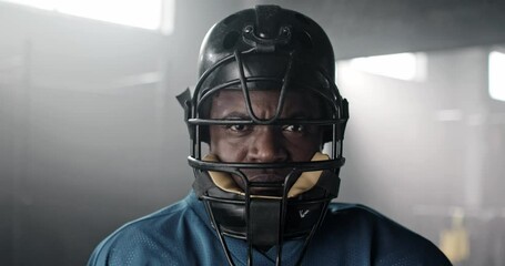 Close-up portrait of serious angry African-American rugby player standing in gym wearing helmet looking at camera. Strong African mad American football athlete in uniform after tiring training.