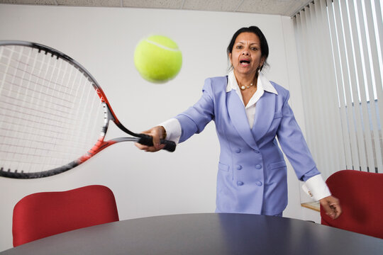 Portrait of a businesswoman playing tennis in an office.