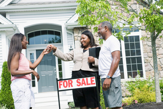 Real estate agent giving key to a middle-aged woman in front of a house and smiling