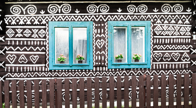 Two blue wooden windows on the White and black pattern ornament painting on the dark wood wall in Slovakian old village Cicmany. European history heritage and black and white background concept image.