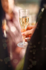 New Year's blurred festive background with a man's hand with a glass of champagne and bokeh from fireworks. wedding champagne party. the groom in a suit holds a glass of champagne in his hand. blurry