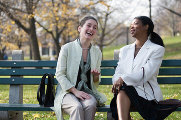 Two women sitting on a bench in the park and laughing.