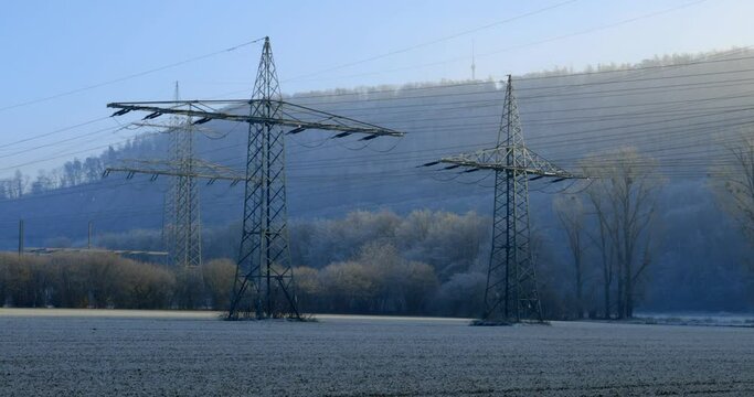W&uuml;rgassen, Germany - 12/17/2022: High-voltage pylons with overhead lines in the evening in the wind on a field with ice