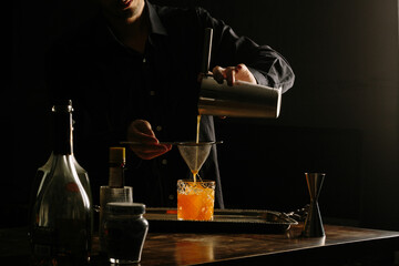 male bartender pouring a cocktail with a cocktail shaker straining into a rocks glass