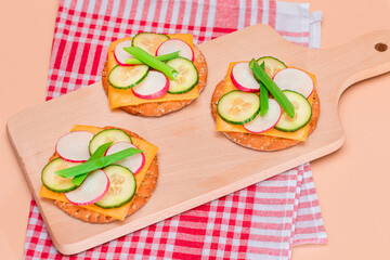Light Breakfast. Quick and Healthy Sandwich. Fresh Cucumber and Radish with Green Onions and Cheese on Crispy Cracker on Wooden Cutting Board