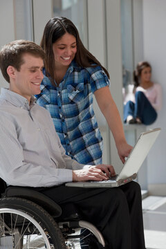 Teacher with spinal cord injury using a laptop with a student standing beside him