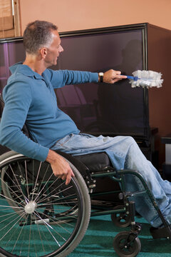 Man with spinal cord injury in a wheelchair dusting furniture