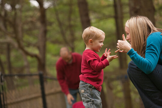 Woman signing the word 'Play' in American Sign Language while communicating with her son in a park