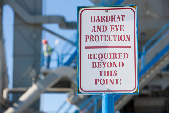 Warning sign saying 'Hardhat and Eye Protection Required Beyond This Point' at an industrial plant