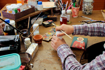 For protection wooden picture is process of applying сraquelure varnish on the product. Reproduction of the icon of St. Nicholas. Workflow of the artist in the studio. Brushes and paints on the backgr