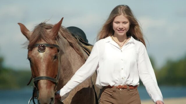 Beautiful equestrian female rider walking charming animal. Close-up shot of caucasian woman training her brown horse along the shore. High quality 4k footage