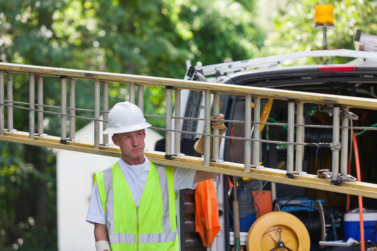Communications worker carrying a ladder from truck to make installation