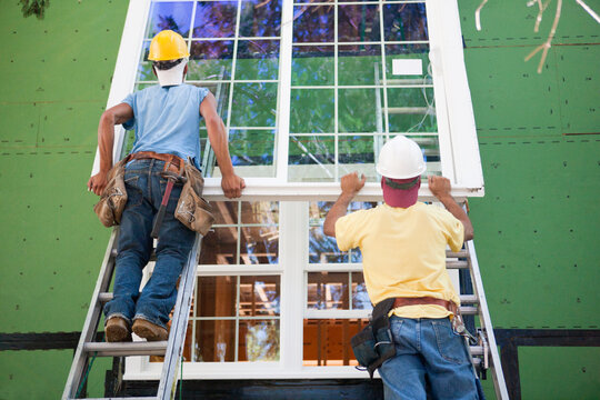Carpenters positioning a large window frame on a house under construction