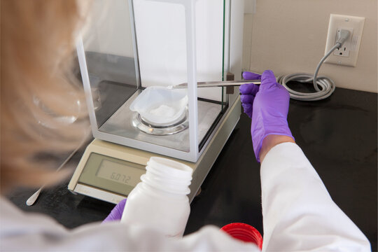 Laboratory scientist adding a small amount of solid reagent to a container on a scale