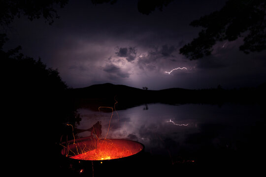 Camping fire pit at night with lightning in the background at Lake Umbagog, New Hampshire, USA