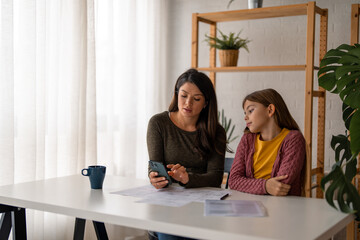 Mother looking at her finances on a online banking app while her daughter sitting next to her...