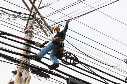 Communications worker on a power pole attaching clips to support cable