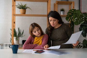 Sometimes a little help is needed. Photo of a worried mother helping her school daughter with homework at home during the day while sitting at the table. - obrazy, fototapety, plakaty
