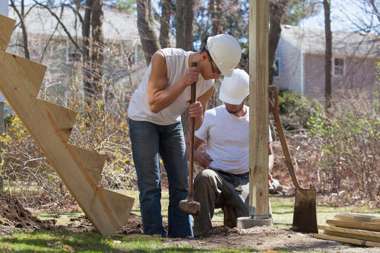 Hispanic carpenters using sledge hammer to tamp dirt at deck footing