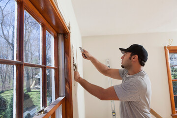 Hispanic carpenter cutting wallboard for new deck doorway in house