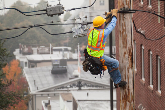 Cable lineman holding onto pole while using lineman spikes to adjust tension